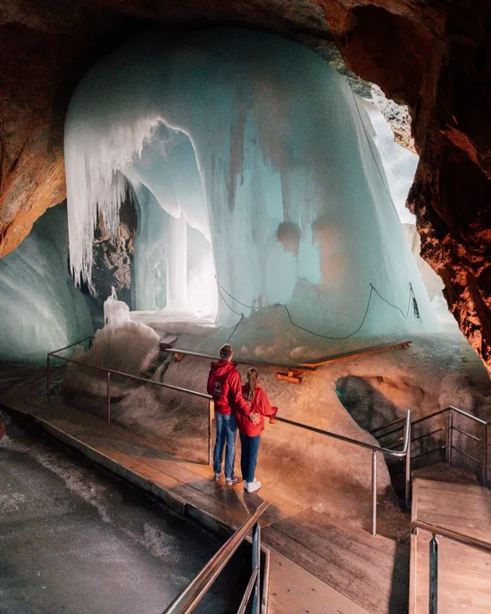 Coppia esplora grotta ghiacciata con grandi formazioni di ghiaccio blu e passerella in legno